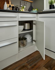 Eckunterschrank in einer modernen Küche, geöffnet, mit Töpfen und Schüsseln auf zwei Regalböden, aus der Perspektive von vorne rechts.