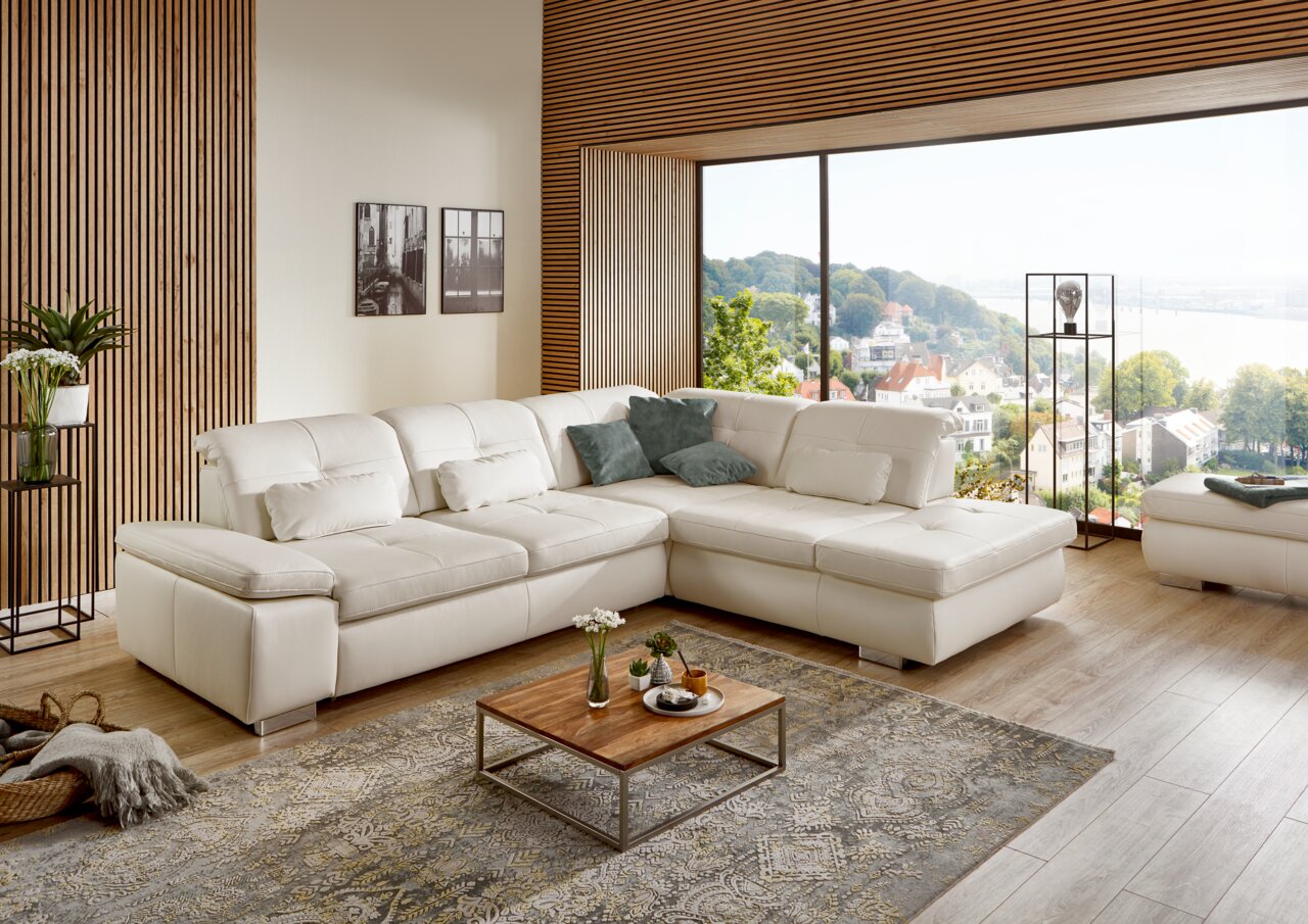 Moderne weiße Eckgarnitur in einem stilvollen Wohnzimmer mit Blick auf eine große Fensterfront und eine malerische Landschaft.