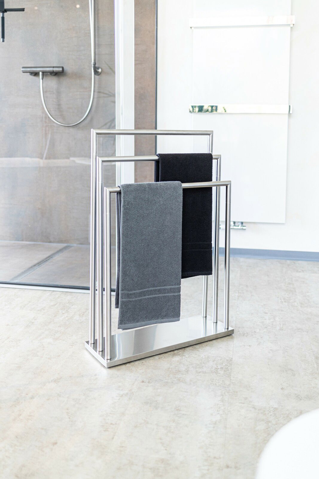Moderner Handtuchständer aus der Serie WALDI von Zurbrüggen, aus Edelstahl mit zwei Handtüchern, in einem Badezimmer mit Blick auf die Duschkabine.