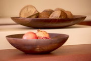 Twee decoratieve donkerbruine houten schalen met granaatappels en natuurlijke noten, vanuit een laag frontaal perspectief gefotografeerd.