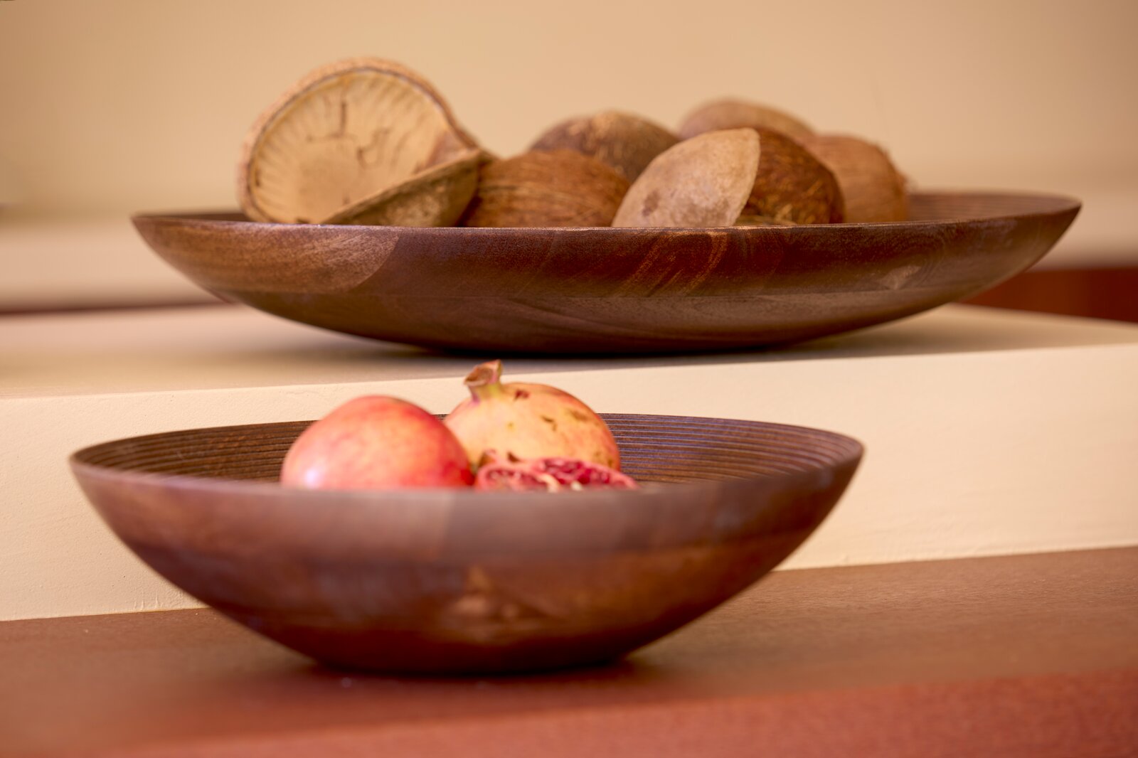 Twee decoratieve donkerbruine houten schalen met granaatappels en natuurlijke noten, vanuit een laag frontaal perspectief gefotografeerd.