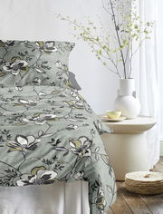 Bettwäsche mit floralem Muster in Grün- und Grautönen, auf einem Bett arrangiert, seitliche Perspektive.