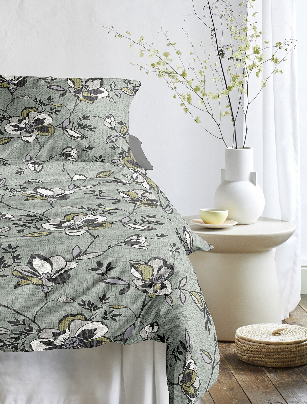 Bettwäsche mit floralem Muster in Grün- und Grautönen, auf einem Bett arrangiert, seitliche Perspektive.