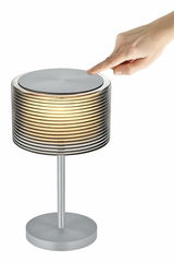 Akku-Tischleuchte GRAND GROVE in seitlicher Perspektive mit einer Hand, die den oberen Teil berührt.