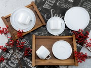 Draufsicht (Flatlay) auf ein weißes Porzellan-Geschirrset mit Tassen, Untertassen und Tellern auf Holztabletts, dekoriert mit roten Beerenzweigen auf einem schwarzen Coffee-Schrift-Hintergrund.