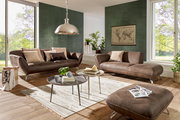 Zwei braune 2-sitzige Sofas in einem modernen Wohnzimmer mit großen Fenstern, grüner Wand und Pflanzen, aus der Frontalperspektive.