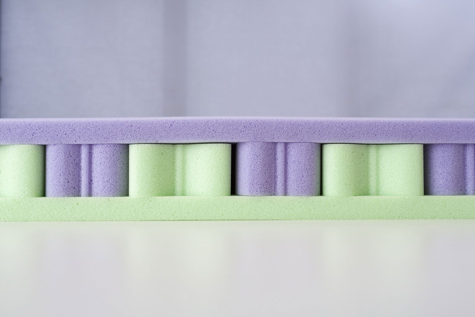 Querschnitt einer Matratze mit lila und grünen Schaumstoffschichten, seitliche Perspektive