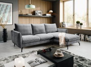 Modernes graues Ecksofa mit rechter Ottomane und schwarzen Metallfüßen in einem hellen Wohnzimmer, fotografiert in frontaler leicht schräger Perspektive.