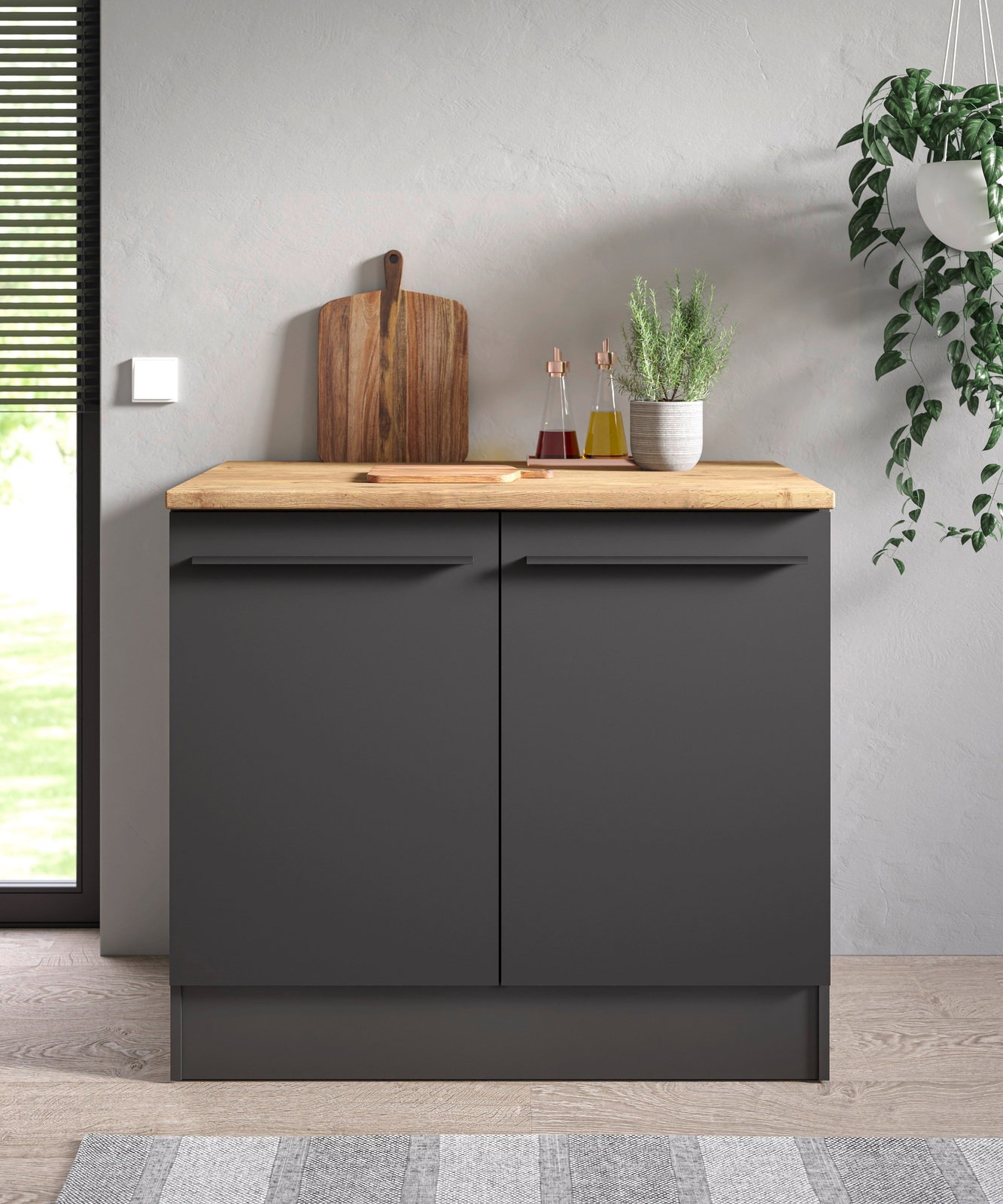 Moderner Spülenunterschrank in dunklem Grau mit Holzarbeitsplatte, frontal fotografiert, dekoriert mit Schneidebrett, Gewürzflaschen und Pflanze.