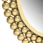 Close-up van een ronde spiegel met gouden bolletjes als versiering van de lijst, vanuit de zijkant in perspectief gefotografeerd.