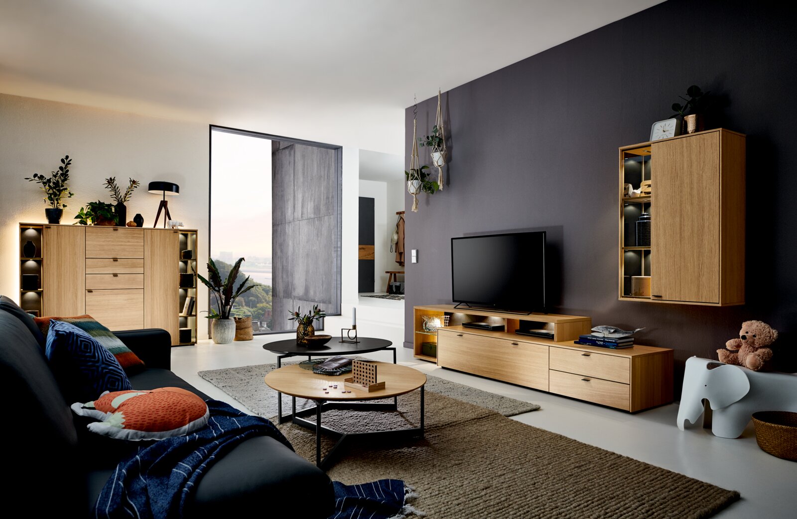 Moderne woonkamer met houten tv-meubel en wandkast met verlichting, gefotografeerd in een brede hoek vanuit de zithoek richting de tv-wand.