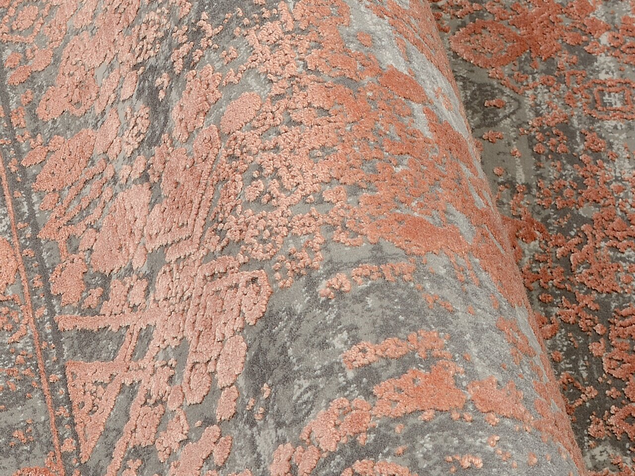 Nahaufnahme eines Designer-Teppichs mit erhabener, floraler Musterung in Rosa auf grauem Hintergrund, seitliche Perspektive