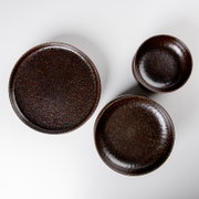 Dreiteiliges Keramikgeschirr-Set in dunklem Braun mit gesprenkelter Glasur (großer Teller, kleiner Teller und Schale), fotografiert in Draufsicht von oben auf weißem Hintergrund