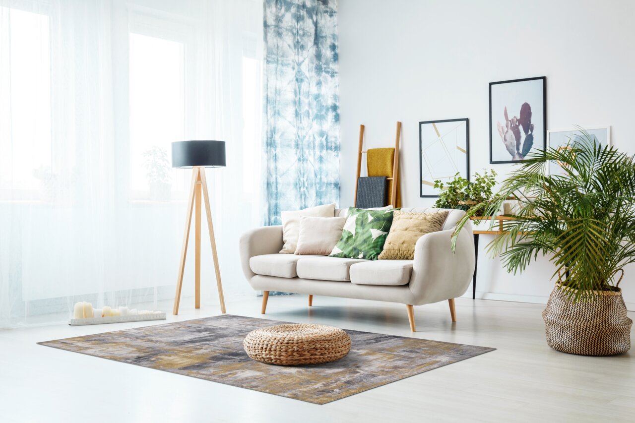 Luxor living Teppich PRIMA Moderner Wohnzimmerteppich in Grau- und Brauntönen, zentral im Raum platziert, mit einem runden, geflochtenen Sitzkissen darauf. Perspektive von vorne.