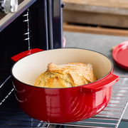 Roter ovaler Gusseisen-Bräter mit Brot im Ofen, seitliche Perspektive