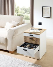 Rollcontainer GLENN mit offener Schublade, seitliche Perspektive, neben einem Sofa platziert, mit Dekorationen wie Buch, Brille und Lampe auf der Oberseite.