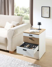 Rollcontainer GLENN mit offener Schublade, seitliche Perspektive, neben einem Sofa platziert, mit Dekorationen wie Buch, Brille und Lampe auf der Oberseite.