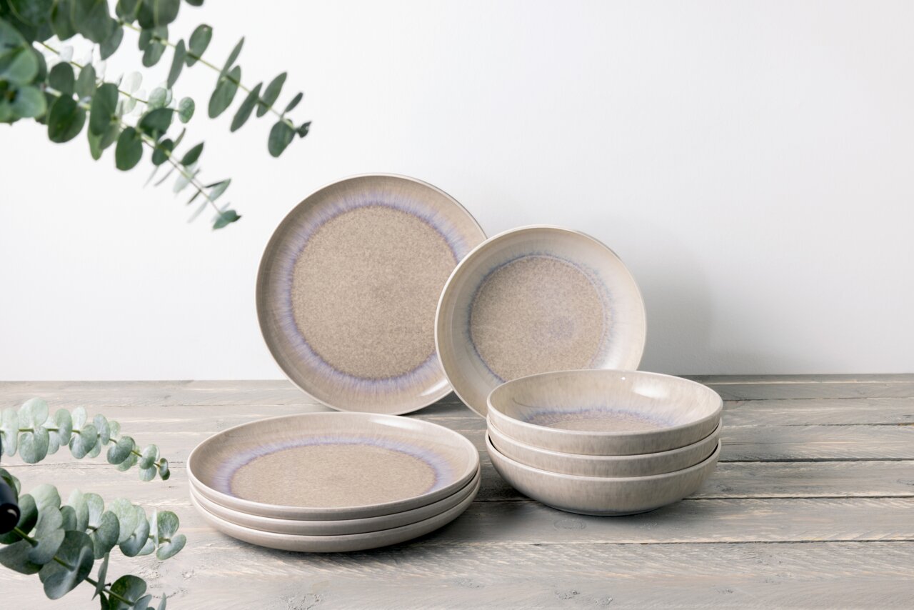 Tafelservice 8-tlg. in natürlichem Design mit sanften Beige- und Blautönen, bestehend aus flachen und tiefen Tellern, auf einem Holztisch arrangiert. Seitliche Perspektive.