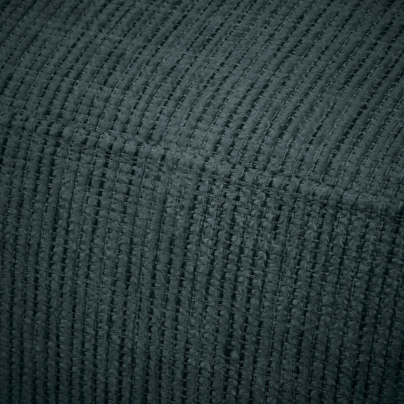 Nahaufnahme eines dunkelgrauen, gerippten Stoffes, perspektivisch von oben fotografiert.
