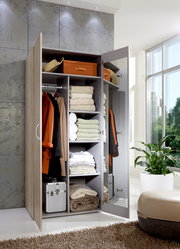 Offener Kleiderschrank mit mehreren Fächern, gefüllt mit Kleidung, Handtüchern und Aufbewahrungsboxen, aus der Perspektive von vorne rechts.