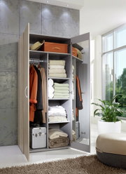 Offener Kleiderschrank mit mehreren Fächern, gefüllt mit Kleidung, Handtüchern und Aufbewahrungsboxen, aus der Perspektive von vorne rechts.