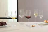 Sechs elegante Weingläser, gefüllt mit verschiedenen Weinsorten, auf einem Tisch arrangiert. Perspektive von vorne.