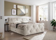 Boxspringbett in einem modernen Schlafzimmer, seitliche Perspektive mit Tageslicht durch ein großes Fenster.