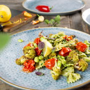Nahaufnahme eines blauen Tellers aus dem Geschirrset Terra 18-tlg. Azur, gefüllt mit einer bunten Gemüse-Pasta, auf einem Holztisch arrangiert.