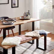 Esszimmer mit Holztisch und Bank, dekoriert mit Sitzkissen aus Schaffell in verschiedenen Farben, seitliche Perspektive