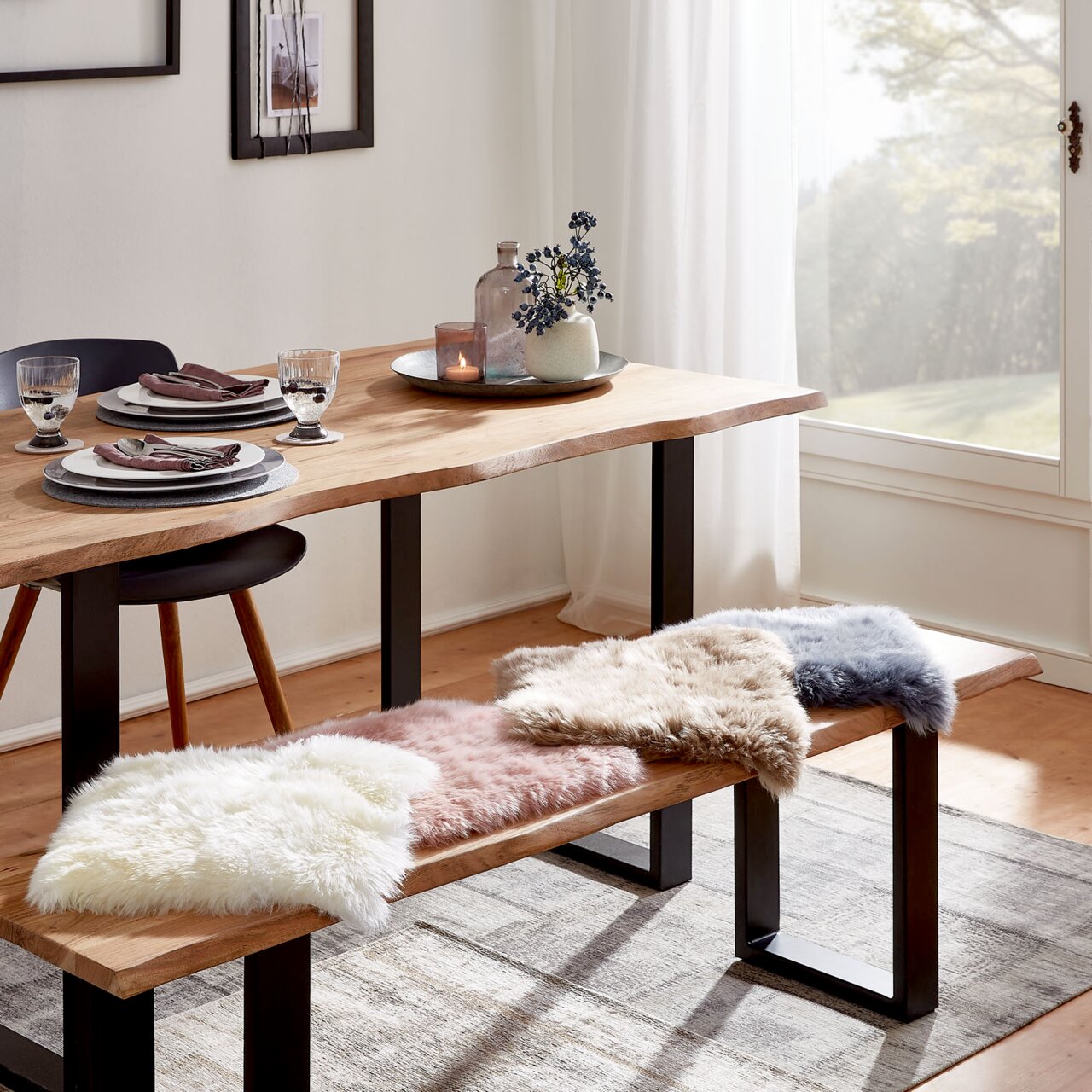 Esszimmer mit Holztisch und Bank, dekoriert mit Sitzkissen aus Schaffell in verschiedenen Farben, seitliche Perspektive