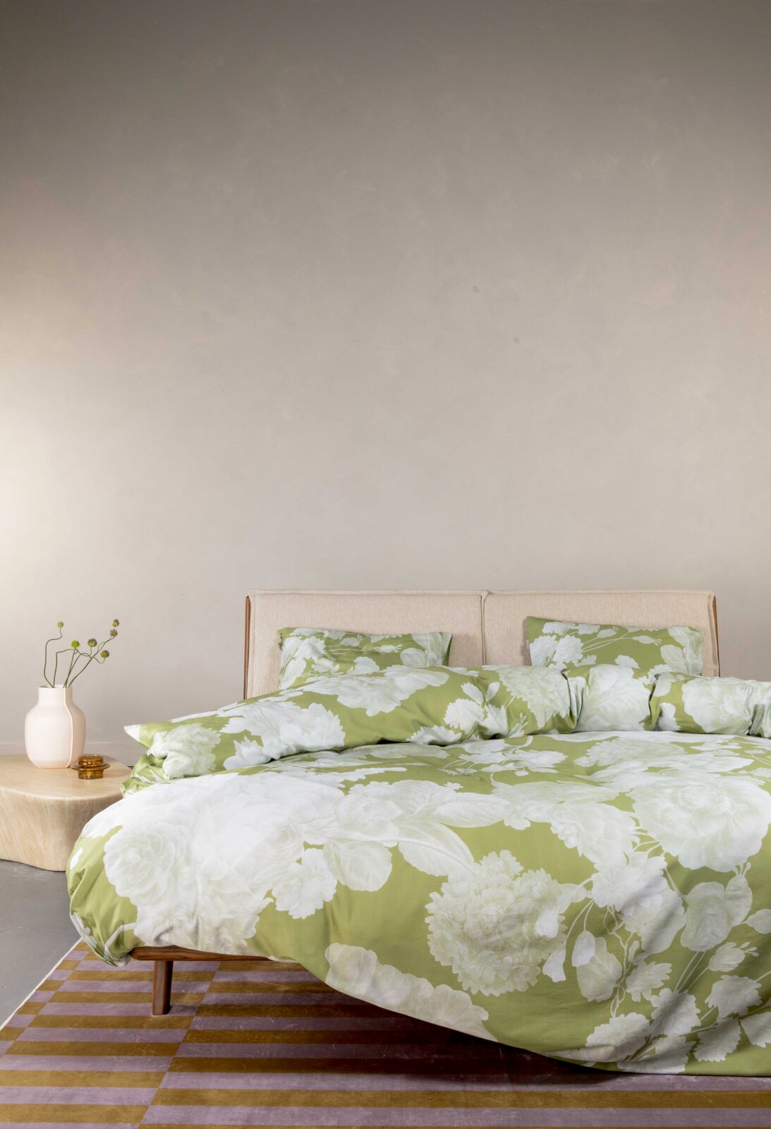 Grün-weißes Bettwäsche-Set mit großflächigem Blumenmuster auf einem Bett mit beigem Kopfteil, frontale leicht seitliche Perspektive