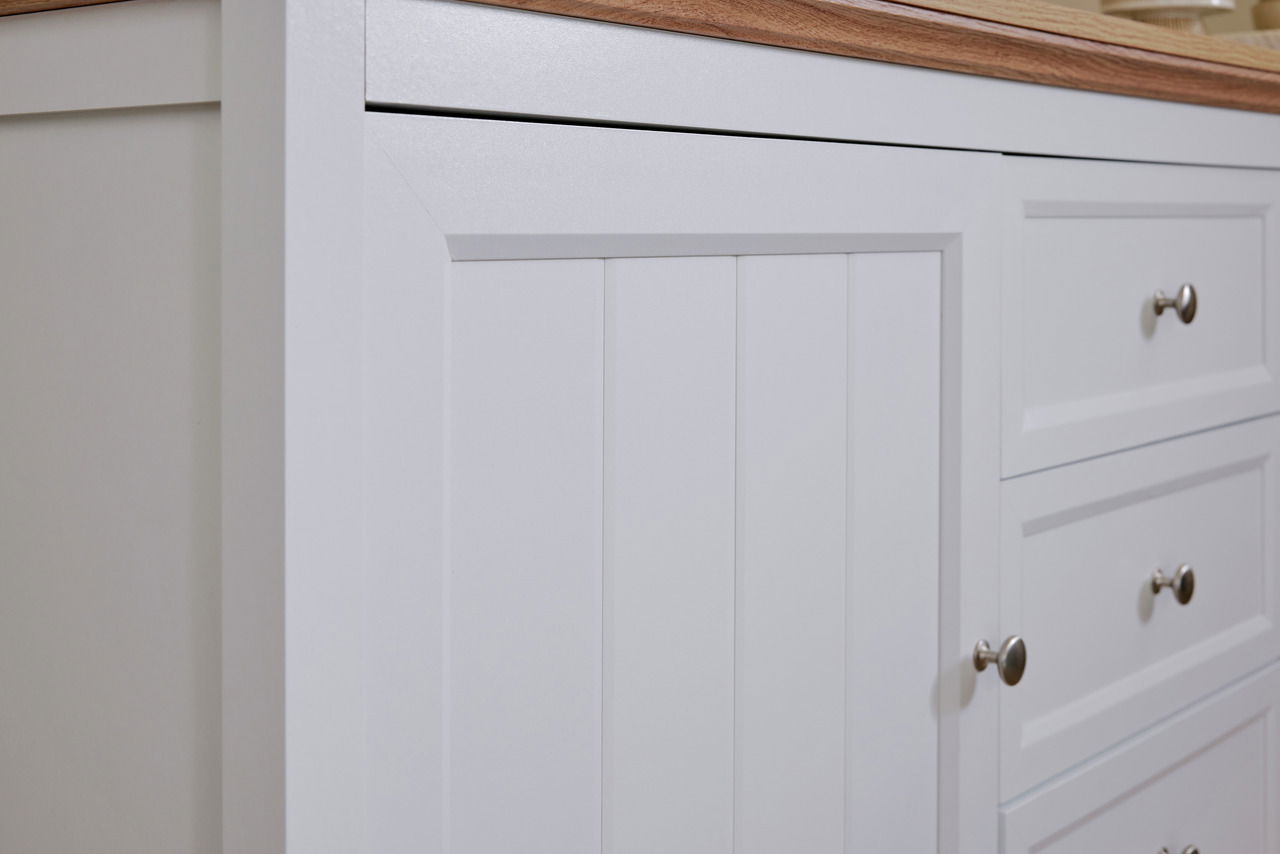 Nahaufnahme eines weißen Sideboards mit Holzplatte, Schubladen und Türen mit silbernen Griffen, seitliche Perspektive.