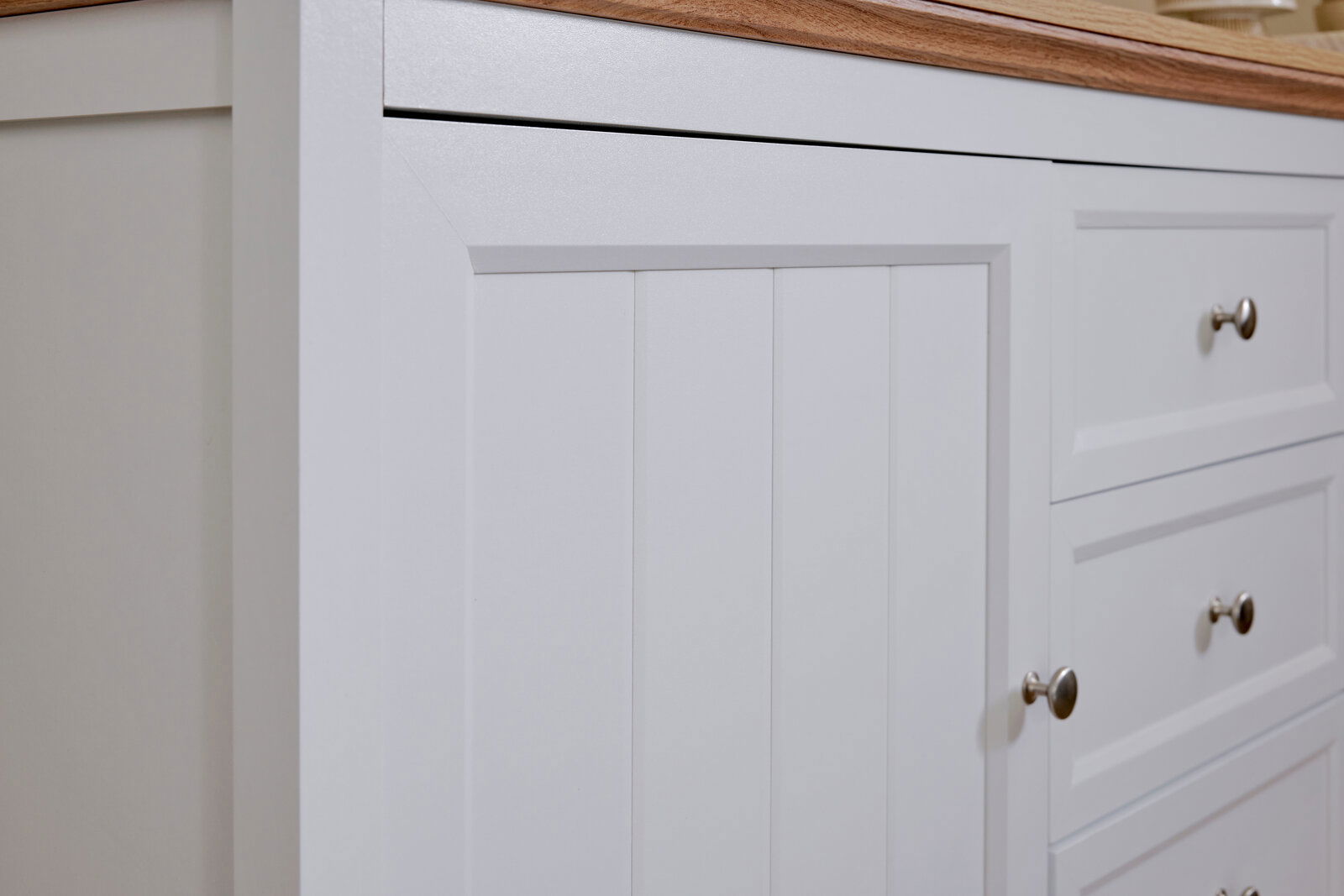 Nahaufnahme eines weißen Sideboards mit Holzplatte, Schubladen und Türen mit silbernen Griffen, seitliche Perspektive.