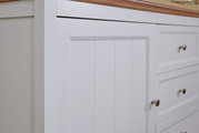 Nahaufnahme eines weißen Sideboards mit Holzplatte, Schubladen und Türen mit silbernen Griffen, seitliche Perspektive.
