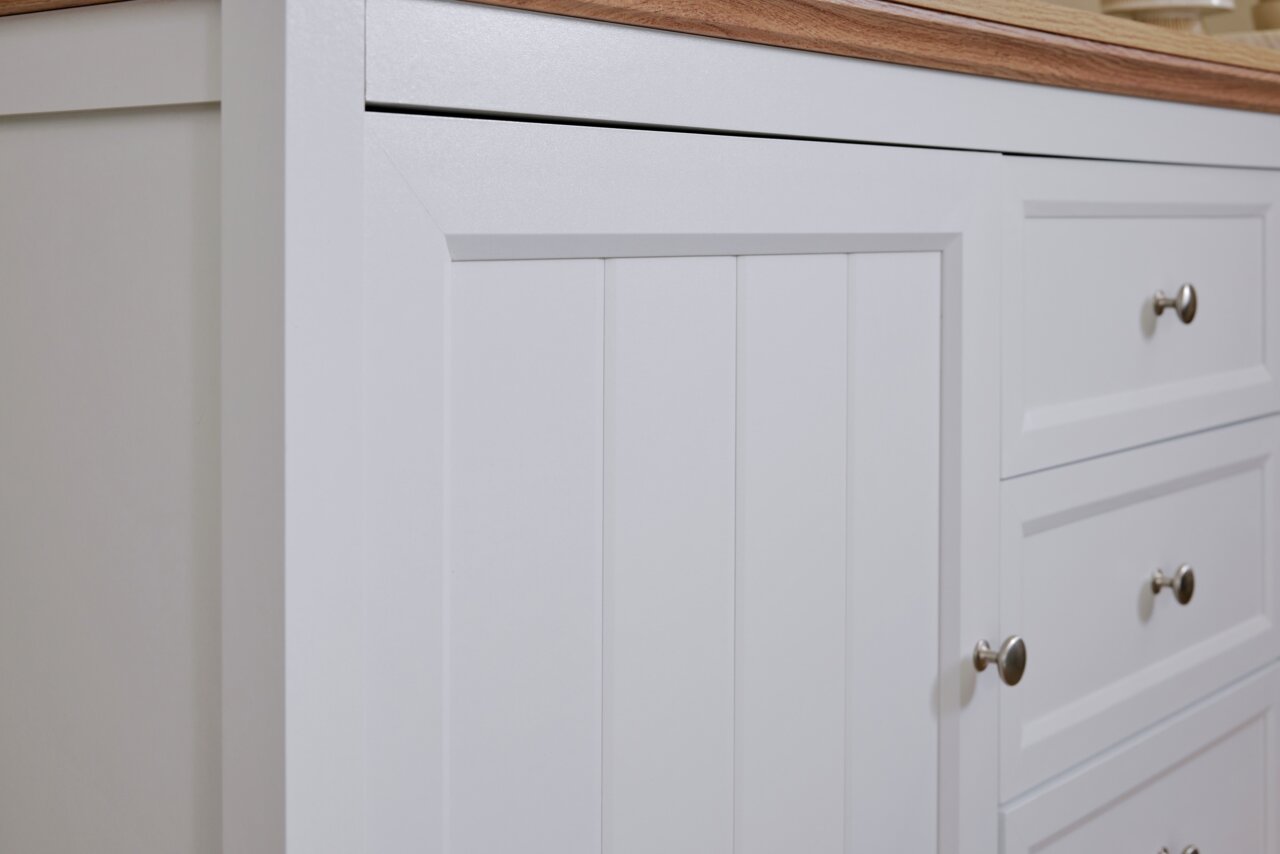 Nahaufnahme eines weißen Sideboards mit Holzplatte, Schubladen und Türen mit silbernen Griffen, seitliche Perspektive.