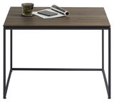 Moderner Beistelltisch mit dunkler Holzplatte und schwarzem Metallgestell, frontal fotografiert. Auf dem Tisch stehen ein Glas, ein Notizbuch und eine zusammengerollte Zeitschrift.