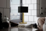 Moderne Tischleuchte PRIME mit schwarzem Schirm und goldfarbenem Sockel, seitlich auf einem Tisch vor einem Fenster platziert.