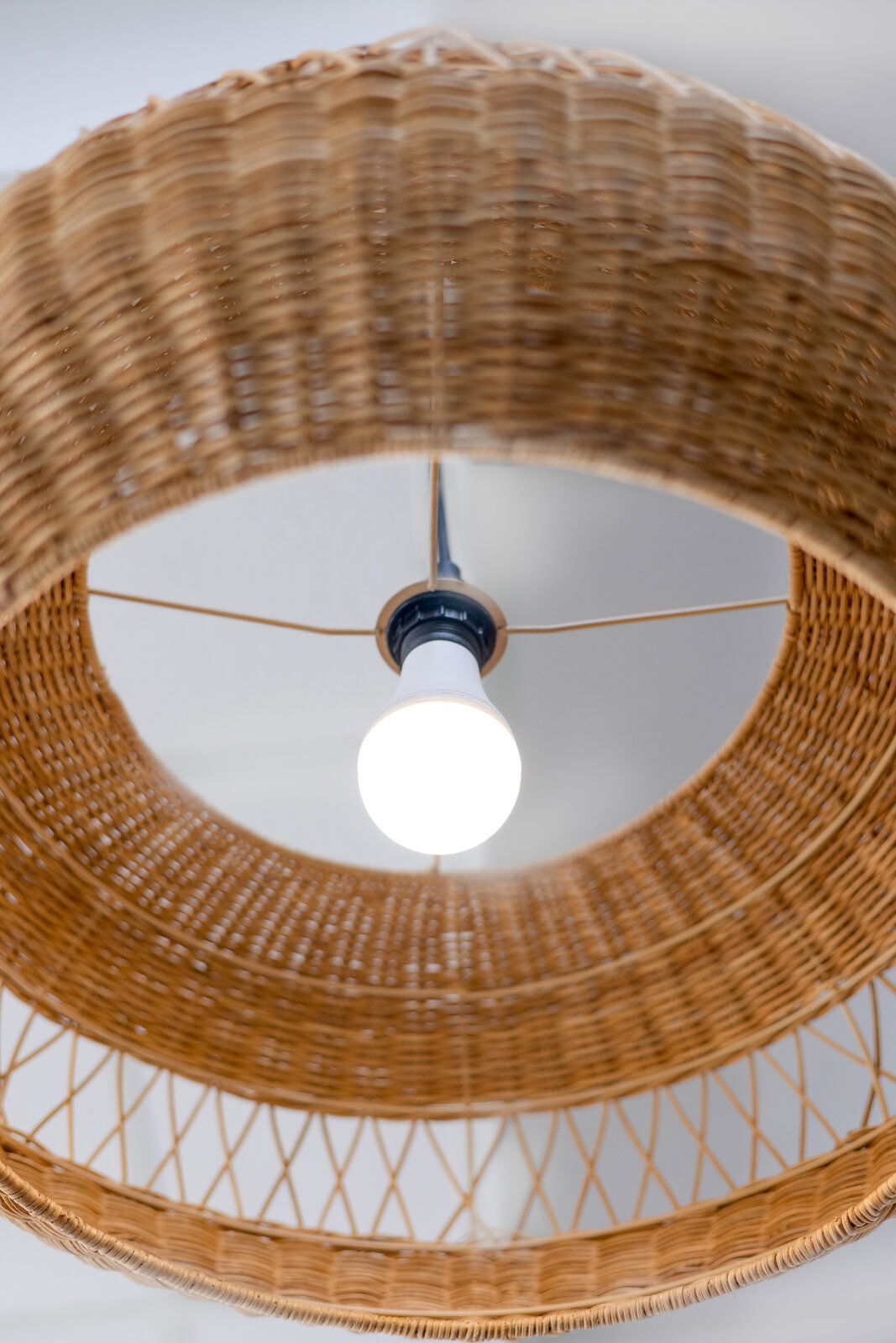 Blick von unten auf eine leuchtende Akku-Glühbirne in einem geflochtenen Lampenschirm.