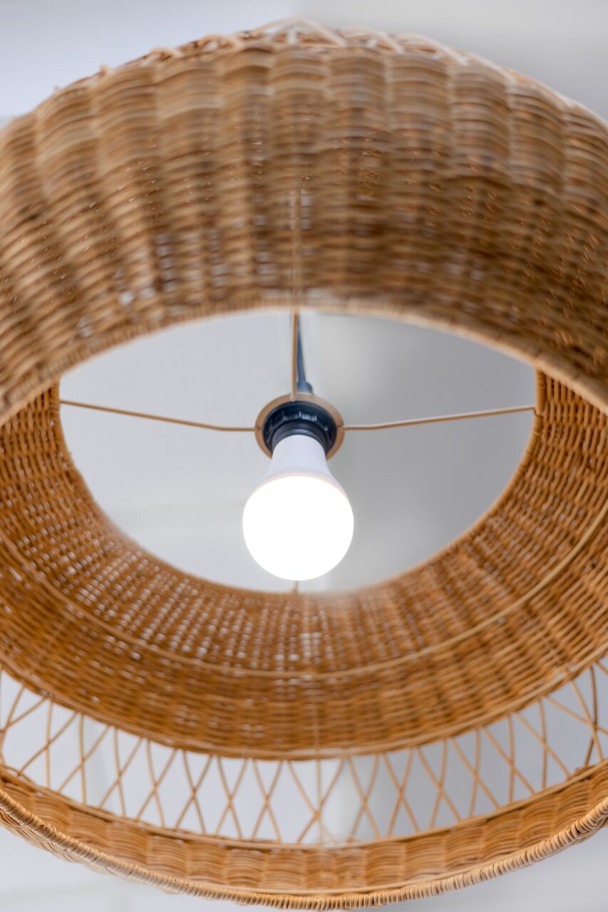Een blik van onderaf op een gloeiende oplaadbare gloeilamp in een gevlochten lampenkap.