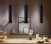 Drie zwarte, cilindervormige hanglampen hangen aan het plafond boven een stijlvol gedecoreerde eettafel. Perspectief: vooraanzicht op de lampen en de tafel.