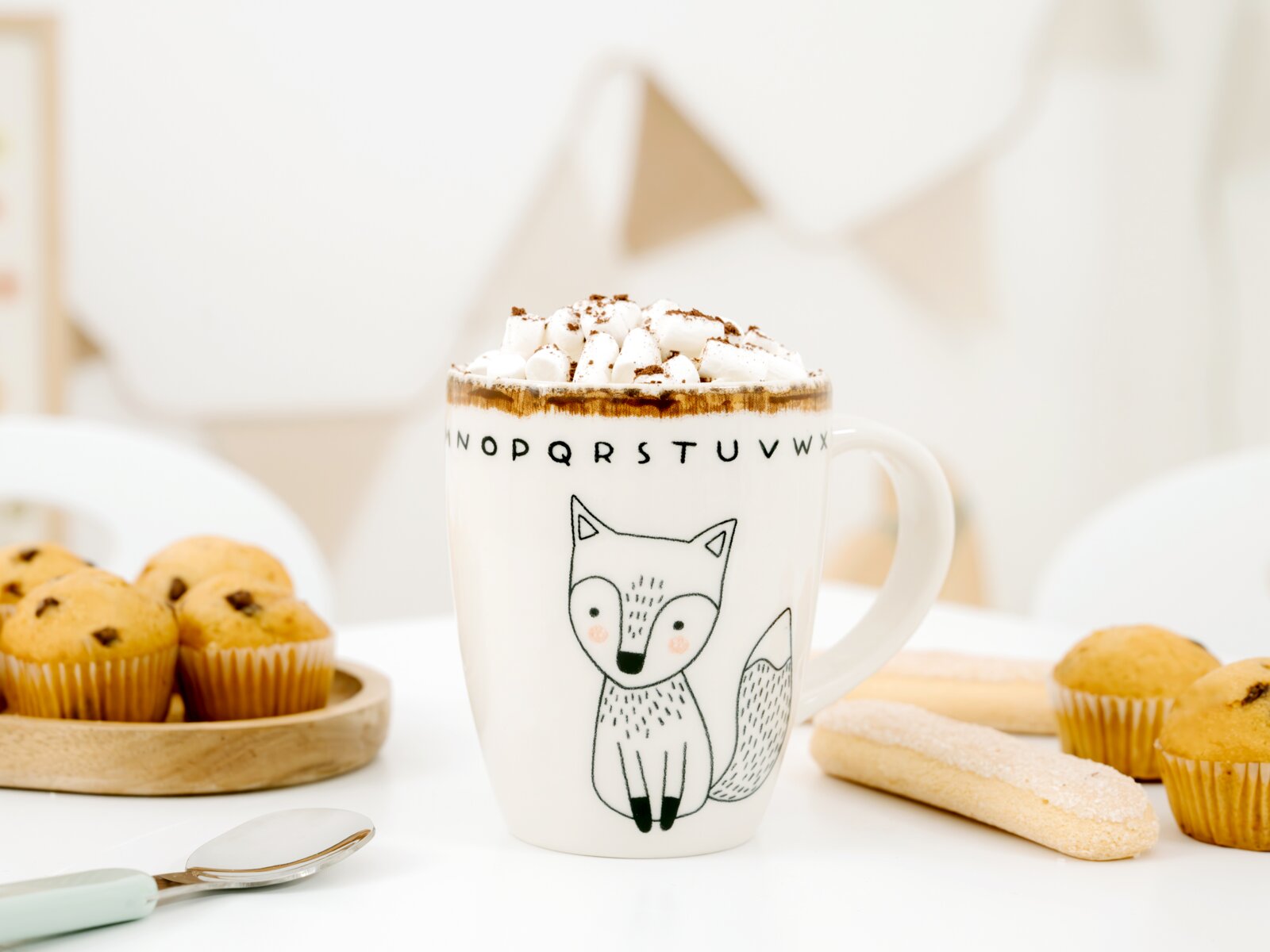 Weiße Keramiktasse mit niedlichem Fuchsmotiv und Buchstabenrand, frontal aus leichter Draufsicht gezeigt, gefüllt mit heißem Kakao und Marshmallows