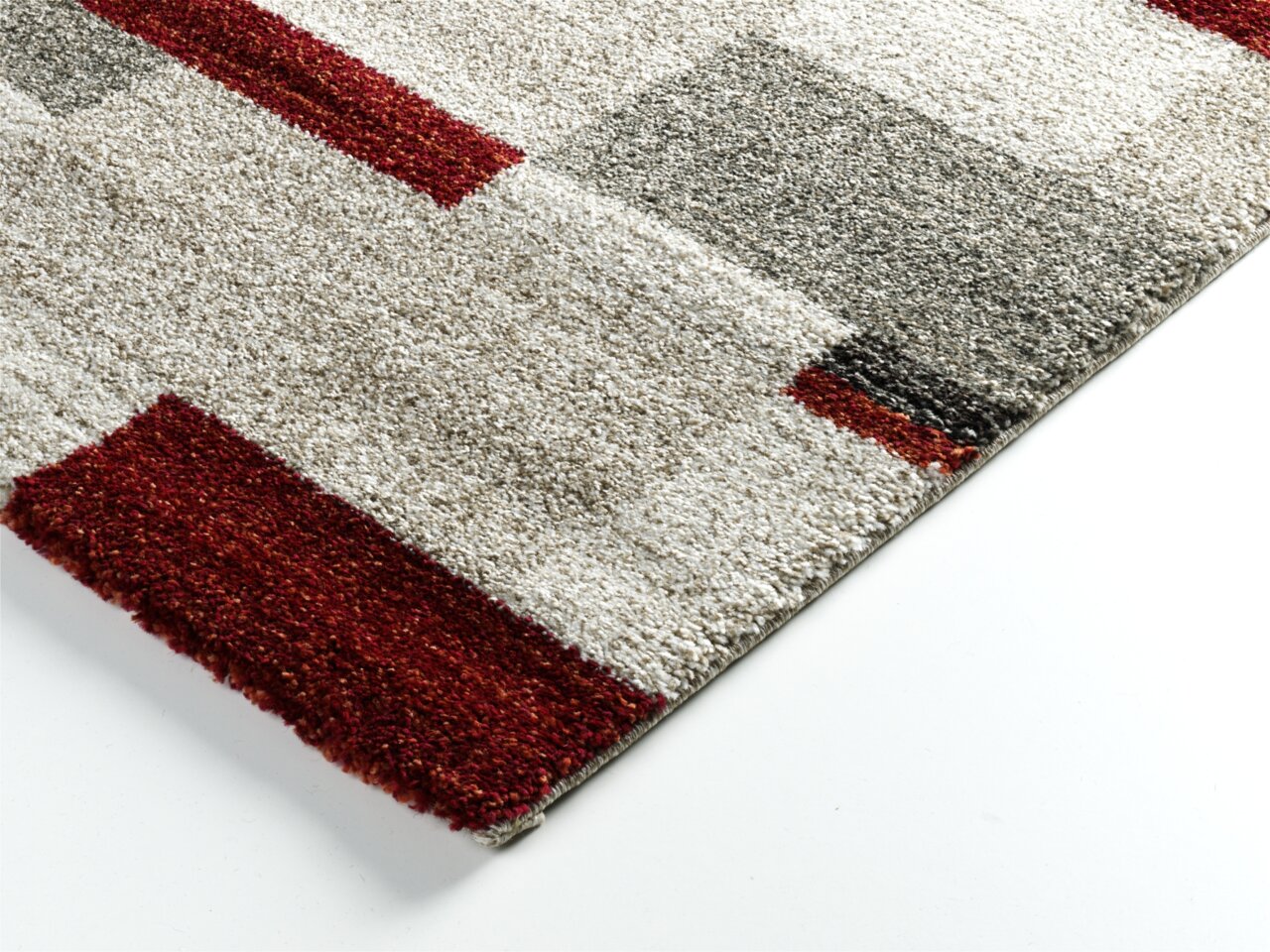 Nahaufnahme eines Teppichs mit geometrischem Muster in Rot, Grau und Beige, perspektivisch von oben fotografiert.