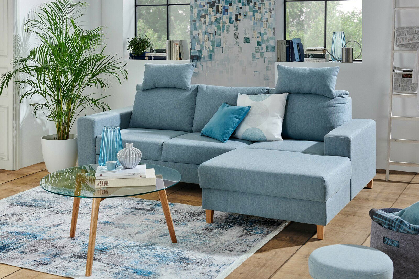 Ti´me Ecksofa ANABELLE Blaue Eckcouch Ti´me Rundecke ANABELLE in einem modernen Wohnzimmer, mit einem runden Glastisch und dekorativen Kissen, aus der Perspektive von vorne rechts.