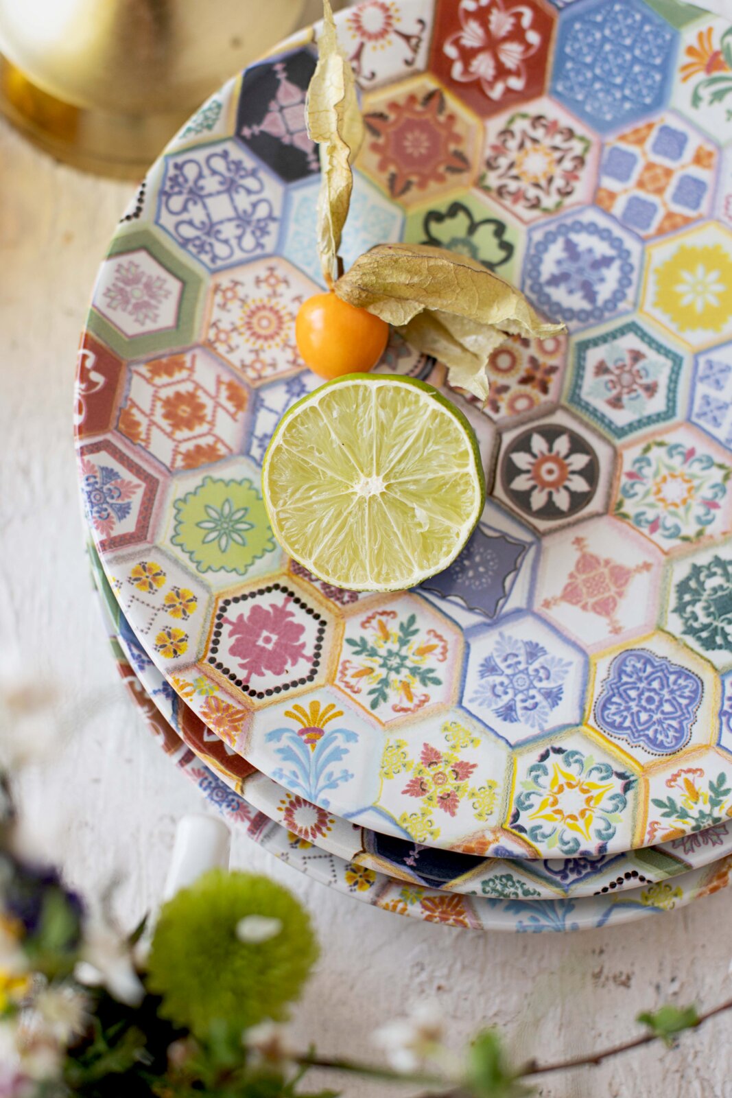 Bunte Keramik-Essteller mit hexagonalem Fliesenmuster in vielen Farben, dekoriert mit einer halben Limette und einer Physalis, aufgenommen in Draufsicht von oben.
