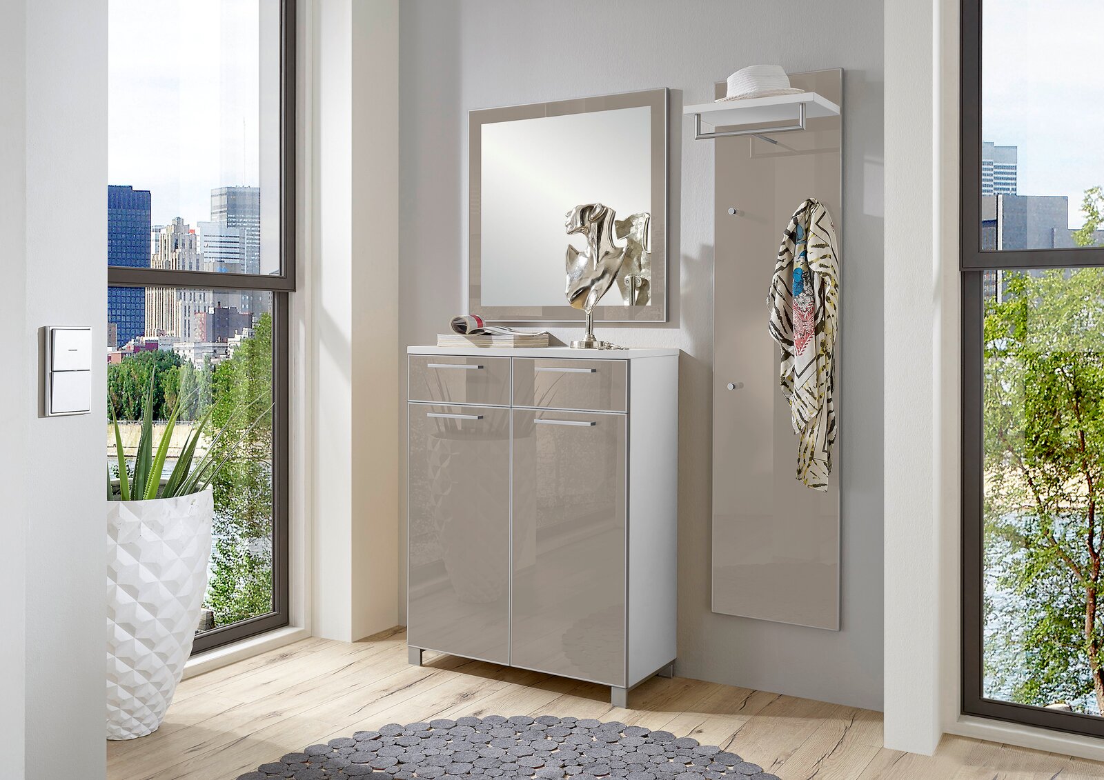 Modernes Garderoben-Set in einem hellen Raum mit großem Fenster, bestehend aus einem Spiegel, einem Schrank und einer Wandgarderobe mit Haken. Perspektive von vorne.