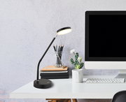 Moderne LED-Tischleuchte in Schwarz auf einem Schreibtisch neben einem Computer, aus seitlicher Perspektive fotografiert.