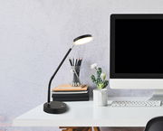 Moderne LED-Tischleuchte in Schwarz auf einem Schreibtisch neben einem Computer, aus seitlicher Perspektive fotografiert.