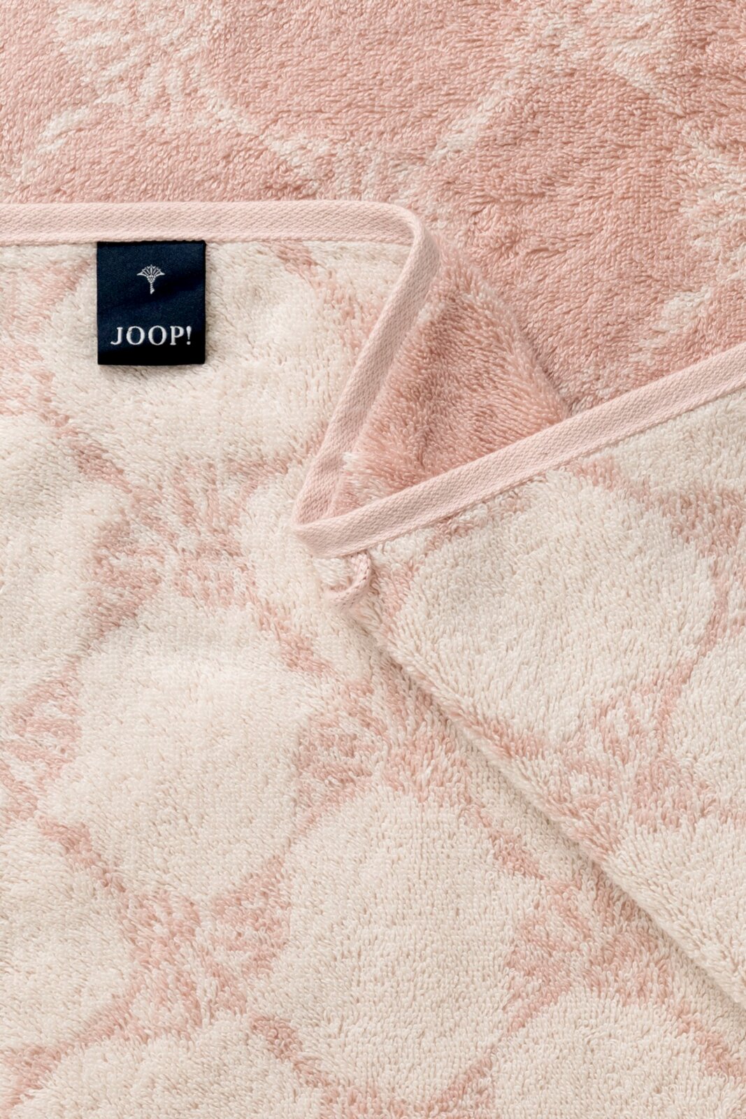 Nahaufnahme eines rosa Gästetuchs mit floralem Muster und einem Joop-Label, von oben betrachtet.