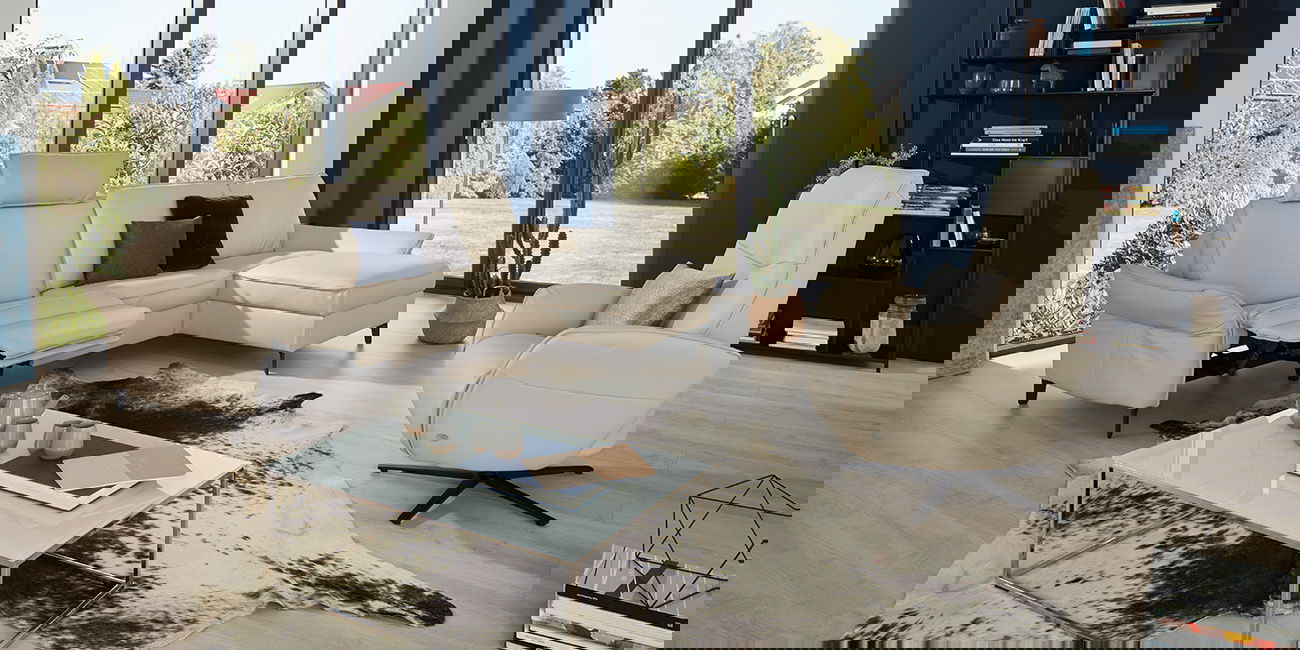 Helles Sofa mit Fußverstellung, großer Teppich und Blick in den Garten.