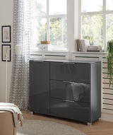 Moderne, dunkelgraue Kommode mit Hochglanzoberfläche, seitliche Perspektive, in einem hellen Raum mit großen Fenstern und dekorativen Elementen.